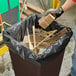 A man putting wood into a black trash can lined with a Lavex Pro heavy-duty garbage bag.