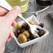 A hand holding a Libbey stainless steel cocktail fork over a bowl of olives.