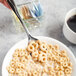 A Libbey stainless steel teaspoon holding a spoonful of cereal over a bowl.