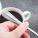 A hand holding a Libbey stainless steel demitasse spoon over a cup of coffee.