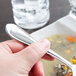 A hand holding a Libbey stainless steel bouillon spoon over a bowl of soup.