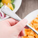 A hand holding a World Tableware stainless steel utility fork over a bowl of pasta.