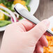 A hand holding a Libbey stainless steel dessert fork over a plate of food.