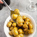 A Libbey stainless steel serving spoon filled with roasted potatoes in a bowl.
