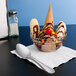 A bowl of ice cream with bananas and chocolate toppings with a Libbey antique stainless steel dessert spoon on a napkin.