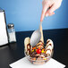 A hand holding a Libbey stainless steel dessert spoon over a bowl of ice cream.