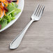 A Libbey stainless steel salad fork next to a plate of salad.