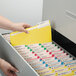 A hand putting a yellow Smead file folder into a file drawer with other folders.