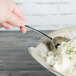 A person using a Libbey stainless steel serving spoon to scoop mashed potatoes.