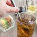 A hand holding a Libbey stainless steel iced tea spoon over a glass of iced tea.