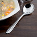 A bowl of soup with a Libbey stainless steel bouillon spoon next to it.