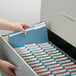 A hand holding a blue Smead file folder in a file cabinet full of files.