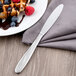 A Libbey stainless steel fluted utility knife on a plate of waffles with berries and chocolate sauce.