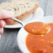 A Libbey stainless steel bouillon spoon filled with soup over a bowl.