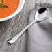 A Libbey stainless steel bouillon spoon on a napkin next to a bowl of soup.