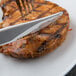 A Libbey stainless steel fluted steak knife and fork on a plate of grilled pork chop.