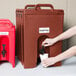 A person pouring a drink from a red Cambro insulated beverage dispenser.