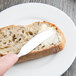 A Libbey stainless steel butter knife spreading butter on a piece of bread.