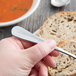 A hand holding a Libbey stainless steel butter knife over slices of bread.