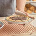 An aluminum pie pan holding a pie with a graham cracker crust and chocolate drizzle.