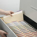 A hand putting a Smead manila file folder into a file drawer with many folders.