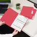 A person holding a red Smead letter size file folder next to a computer.