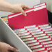 A hand picking up a Smead red letter size fastener folder from a file cabinet.