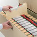 A person's hand opening a file cabinet drawer to put a Smead file folder inside.