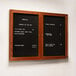 An Aarco cherry-framed bulletin board with black felt and two doors on a wall with a menu.