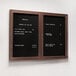 An Aarco walnut frame bulletin board with black felt and hinged doors on a wall with a black and white menu.