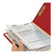 A hand holding a red Smead Heavy Weight Classification Folder with papers.