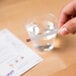 A hand holding a Purell concentration test strip over a glass of water.