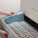 A hand holding a Smead blue file folder opening a file cabinet.