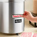 A hand putting a label on an Avantco stainless steel warmer on a hotel buffet counter.