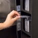 A hand putting a plastic lid into a black vertical countertop T-lid organizer.