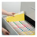 A hand putting a Smead yellow letter size fastener folder into a file drawer.