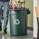 A man putting a trash bag in a Rubbermaid dark green recycling can.