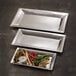 Three American Metalcraft rectangular stainless steel trays with vegetables and dip on a table.