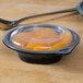 A Fabri-Kal plastic container with oranges in it on a table next to a spoon.