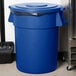 A blue Carlisle Bronco trash can lid with a black handle.