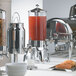 A large silver stainless steel Vollrath juice and beverage dispenser on a hotel buffet table.