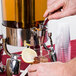 A person using a Vollrath stainless steel juice dispenser to pour a drink into a plastic cup.