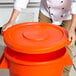 A person holding an orange Carlisle round trash can lid.