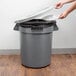 A person opening a Continental Huskee grey trash can with a grey lid to throw away a white plate.