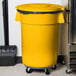 A Carlisle yellow trash can lid on top of a yellow trash can with a black bag.