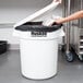 A person putting a black bag into a white Continental Huskee trash can.