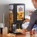 A man using a Carnival King peristaltic cheese sauce dispenser to put cheese on nachos.