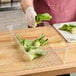 A person in gloves uses a Cambro clear plastic colander pan to cut up lettuce.