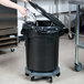 A woman in a black shirt puts foil in a black Rubbermaid BRUTE trash can with a black lid.