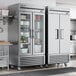 A room in a professional kitchen with two True 2 section glass door reach-in refrigerators.